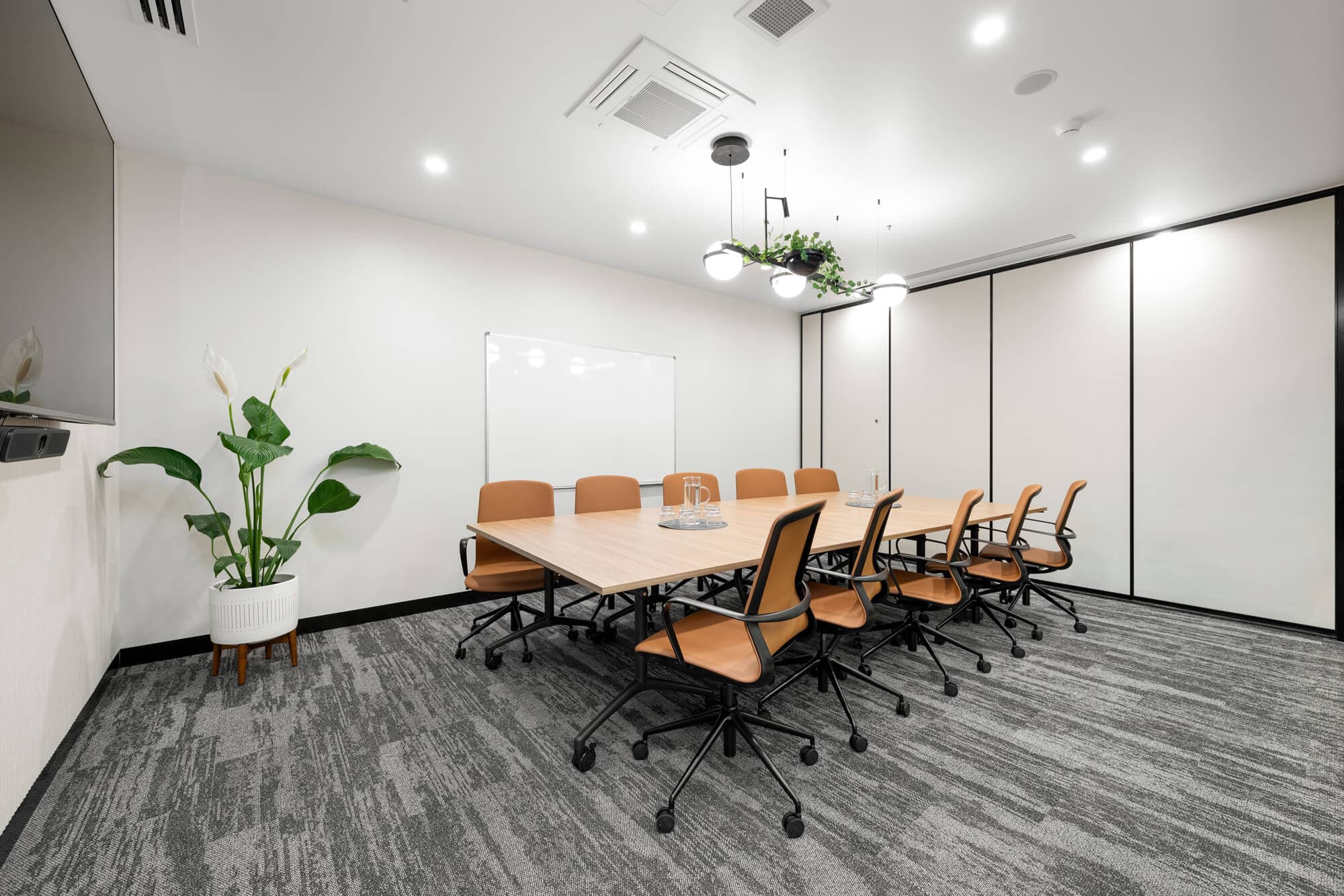 Modern boardroom with light wood table, brown chairs, whiteboard, and gray carpet. Bright, professional meeting space.